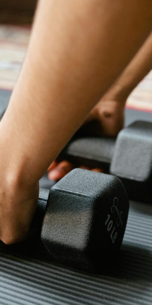Close-up of a person picking up two black 10-pound dumbbells from a textured exercise mat.