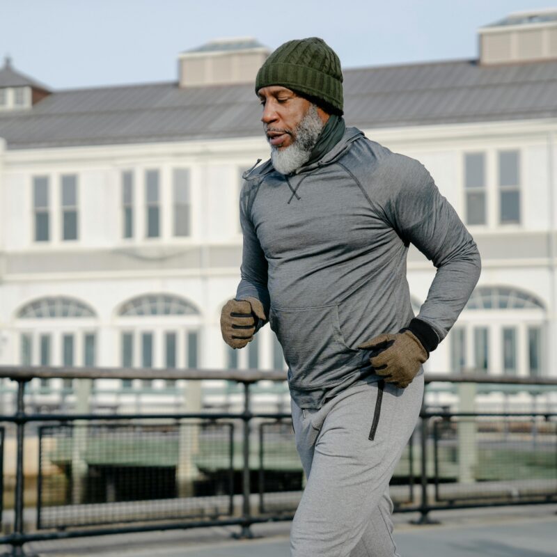 A man jogging outdoors in cold weather, dressed in warm layers, gloves, and a knit hat, demonstrating how to exercise in winter while staying comfortable and active.