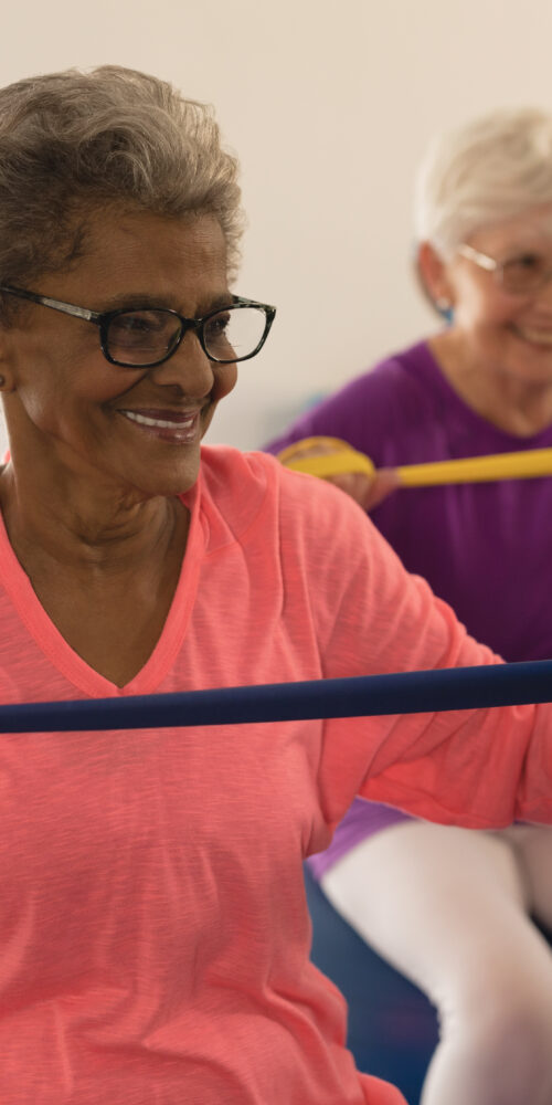 Three elderly patients sitting on exercise balls and using resistance bands for geriatric physical therapy exercises.