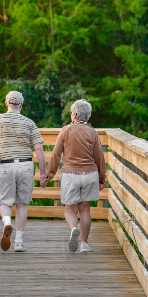 An elderly couple walks along a wooden boardwalk trail, representing a simple way to build healthy habits that stick.