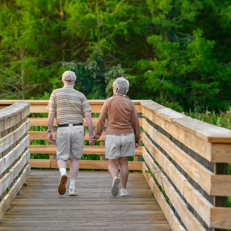 An elderly couple walks along a wooden boardwalk trail, representing a simple way to build healthy habits that stick.