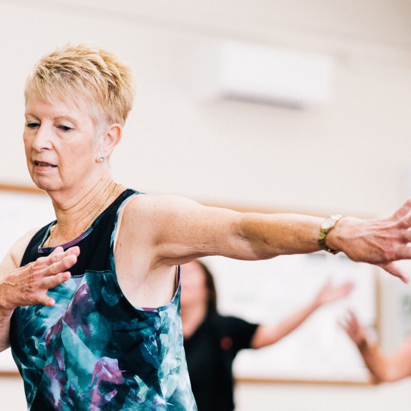 A senior woman in an athletic tank top does an aerobic exercise in a physical rehabilitation center.
